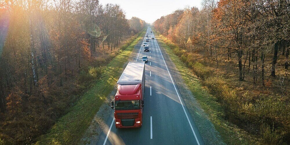 Red shipping truck moving along highway on autumn day